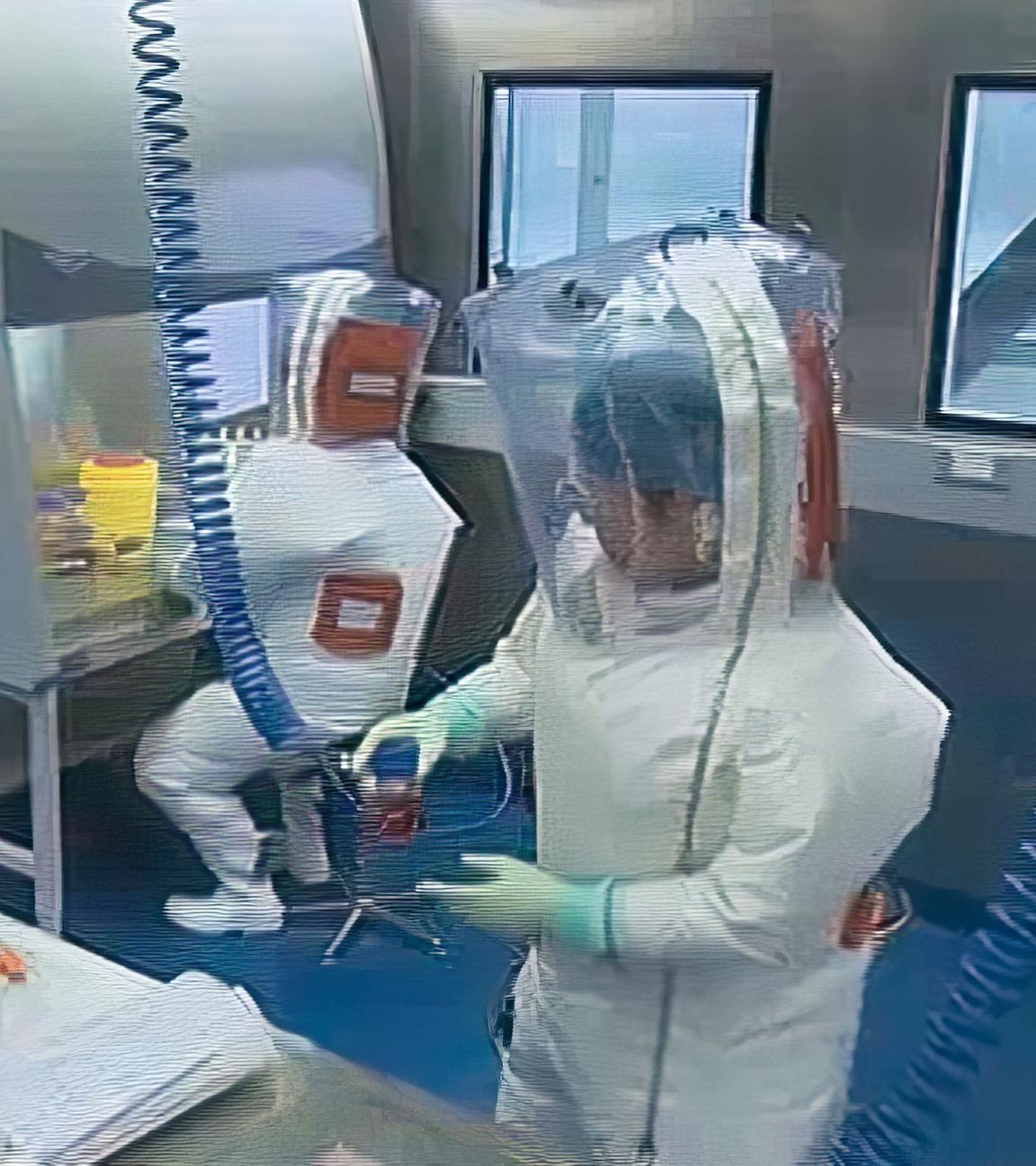 Drei Männer in Schutzkleidung befinden sich in einem Labor.