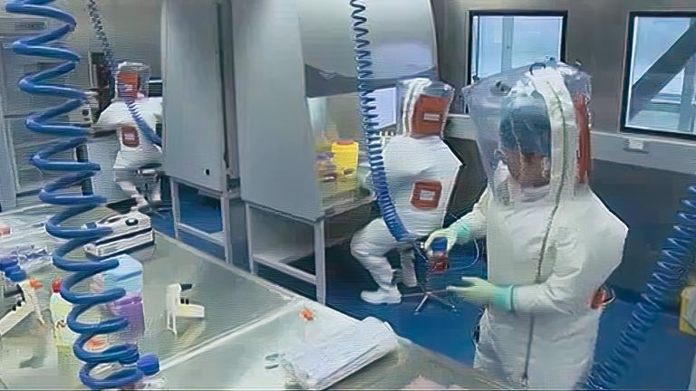 Drei Männer in Schutzkleidung befinden sich in einem Labor.