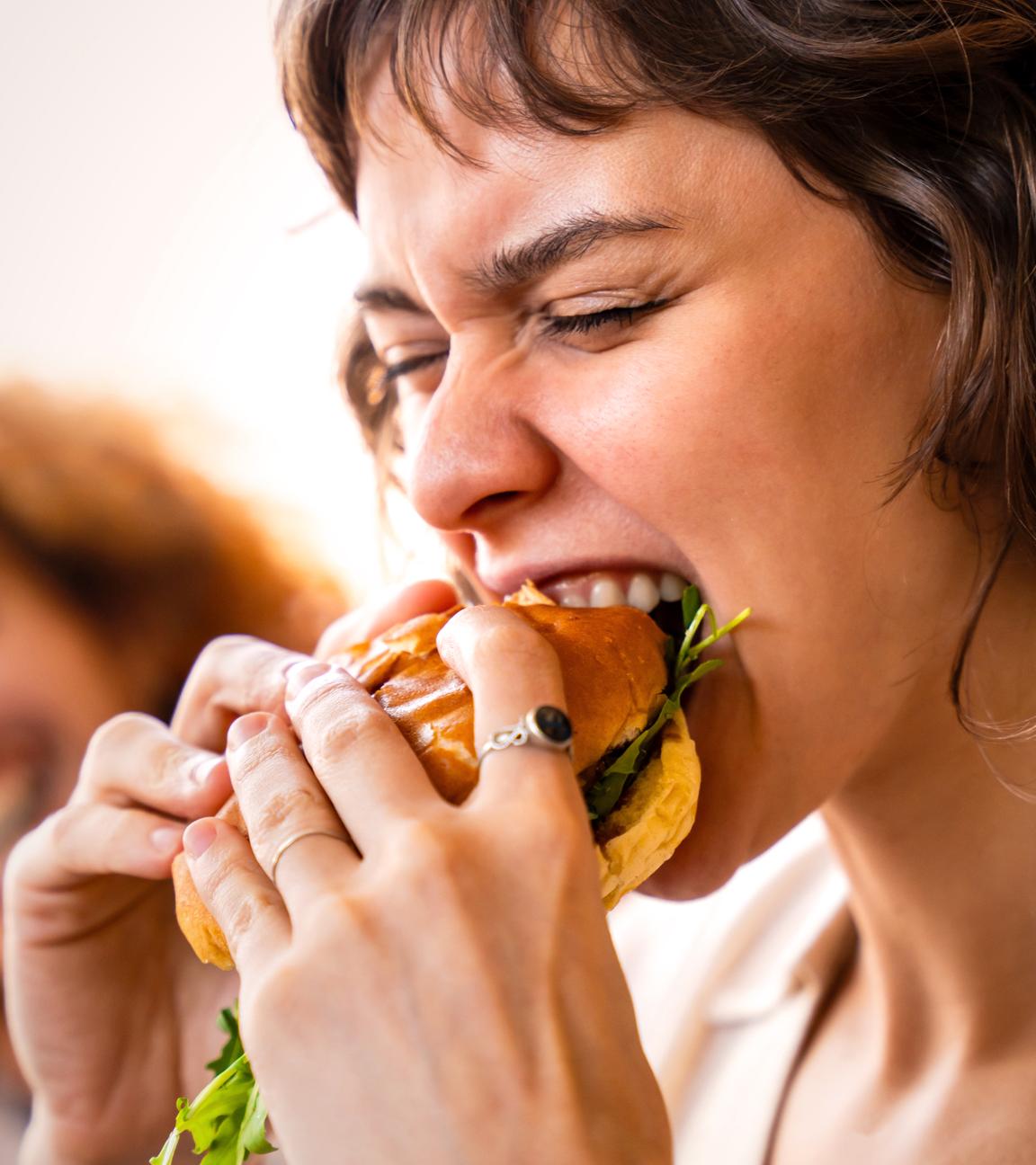 Nahaufnahme, eine junge Frau beißt leidenschaftlich in einen großen Burger