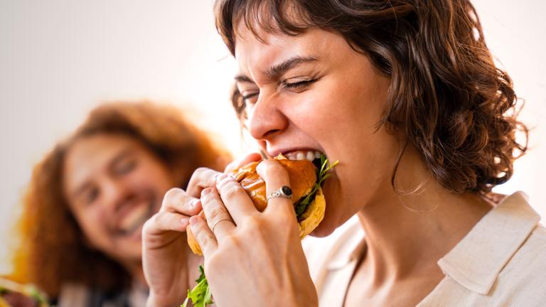 Nahaufnahme, eine junge Frau beißt leidenschaftlich in einen großen Burger