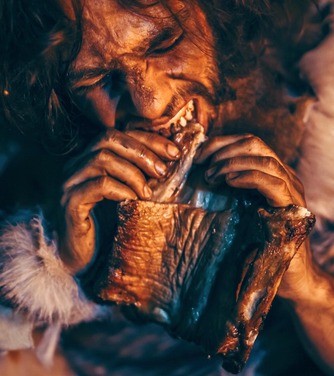 Nahaufnahme, ein Höhlenmensch beißt von einem großen Stück Fleisch ab