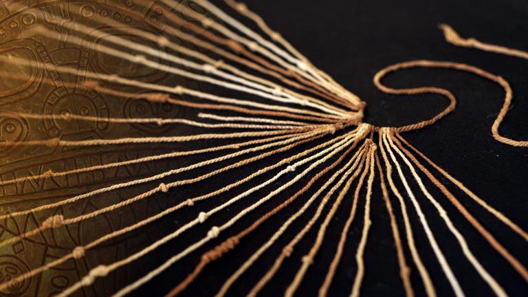 Die Nahaufnahme eines Knotenbändchens der Inka liegt vor schwarzem Hintergrund. An der Seite überlagert das Muster einer Sonnenscheibe der Inka das Foto.