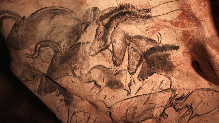 Zeichnungen von Pferden und büffelähnlichen Tieren in schwarz befinden sich auf einer unebenen Felswand.