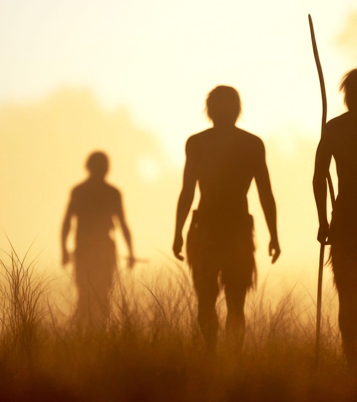 Eine Gruppe Urzeitmenschen in der Steppe, im Gegenlicht sind nur ihre Konturen zu erkennen