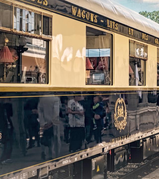 Ein Waggon des Orient-Express an einem Bahnhof; an den Bildrändern leichte Überblendung mit einer alten Landkarte.