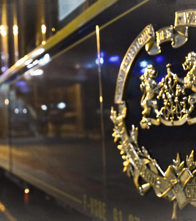 Ein Waggon des Orient-Express an einem Bahnhof, bei Nacht; an den Bildrändern leichte Überblendung mit einer alten Landkarte.