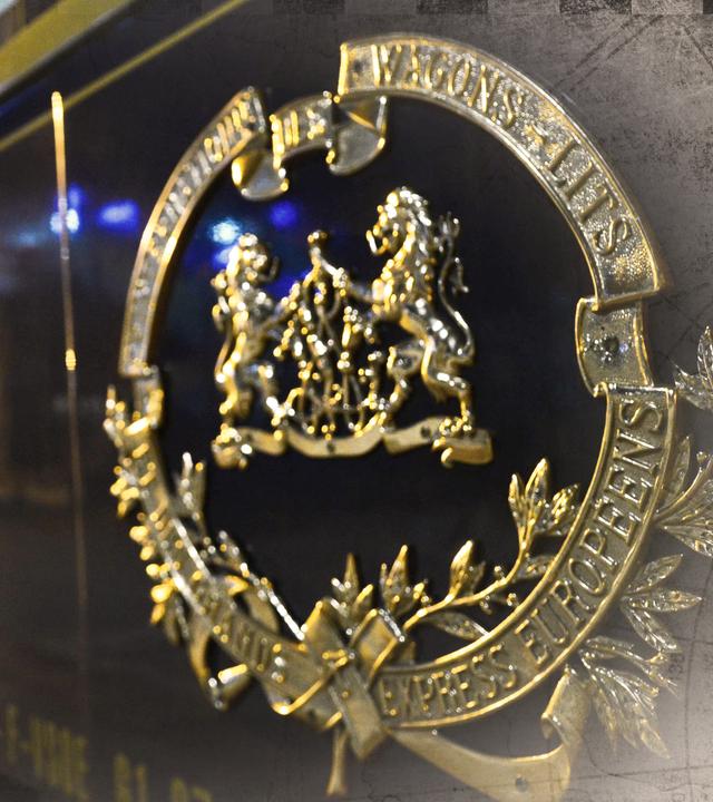 Ein Waggon des Orient-Express an einem Bahnhof, bei Nacht; an den Bildrändern leichte Überblendung mit einer alten Landkarte.