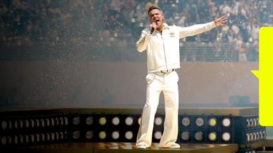 Robbie Williams performt in weißem Anzug auf der Bühne.