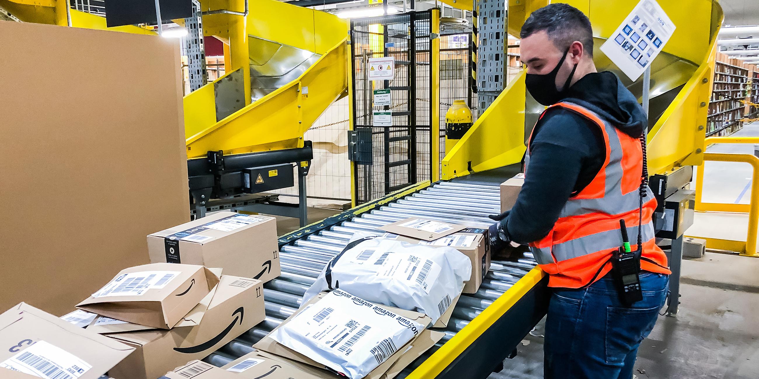Die Packstraße im Amazon-Logistikzentrums Brieselang. Ein Mitarbeiter steht am Förderband und achtet darauf, dass sich nichts verheddert.