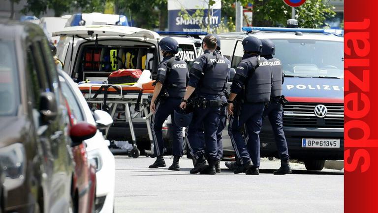 Polizisten am Tatort, zwischen einem Polizeiauto und einer Rettungsliege.