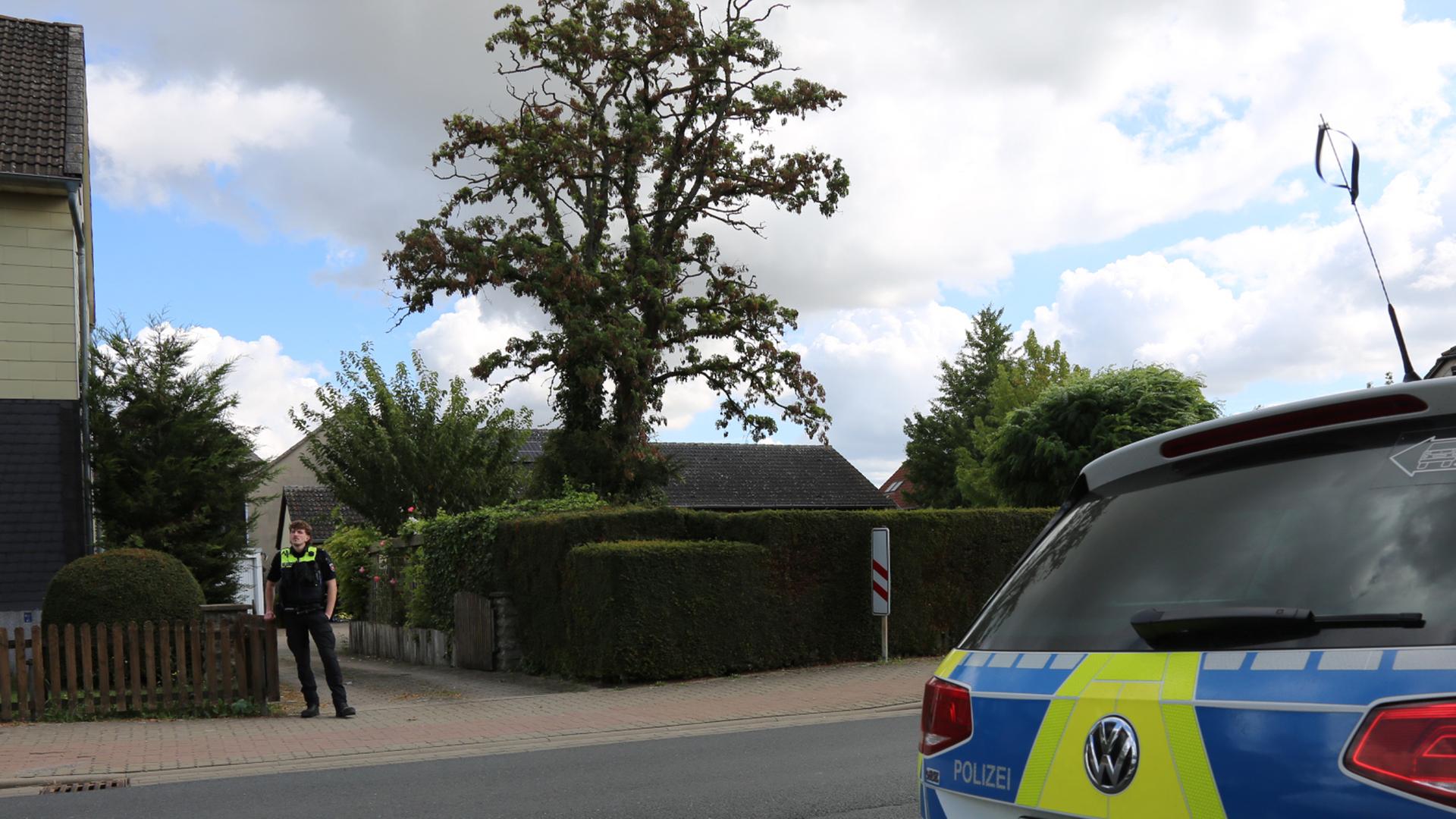 30.08.2025, Niedersachsen, Wolfenbüttel: Ein Polizist und Streifenwagen stehen vor einer Einfahrt. 