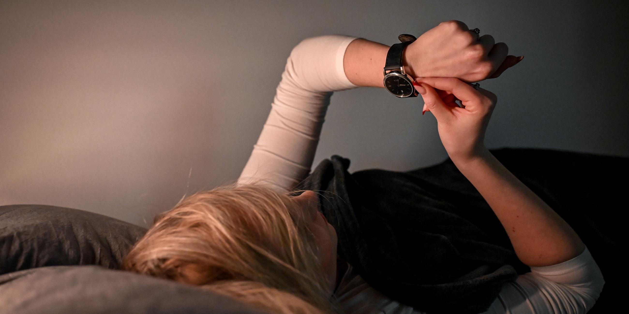In Frau liegt im Bett und und stellt die Zeit an ihrer Armbanduhr ein.