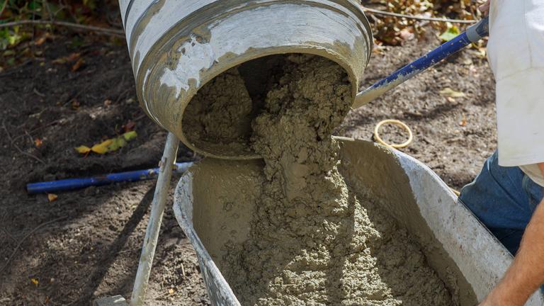 Zement fließt aus einem Betonmischer in eine Schubkarre.