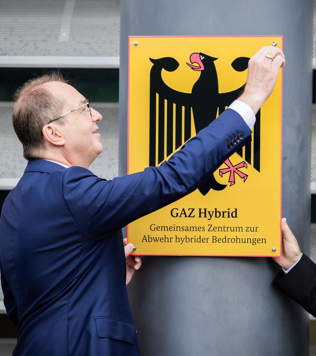 Alexander Dobrindt (CSU, l), Bundesinnenminister, schraubt im Beisein von Sinan Selen, Präsident des Bundesamtes für Verfassungsschutz, posieren symbolisch bei der Einweihung des Gemeinsamen Zentrums zur Abwehr hybrider Bedrohungen das entsprechende Schild an. 