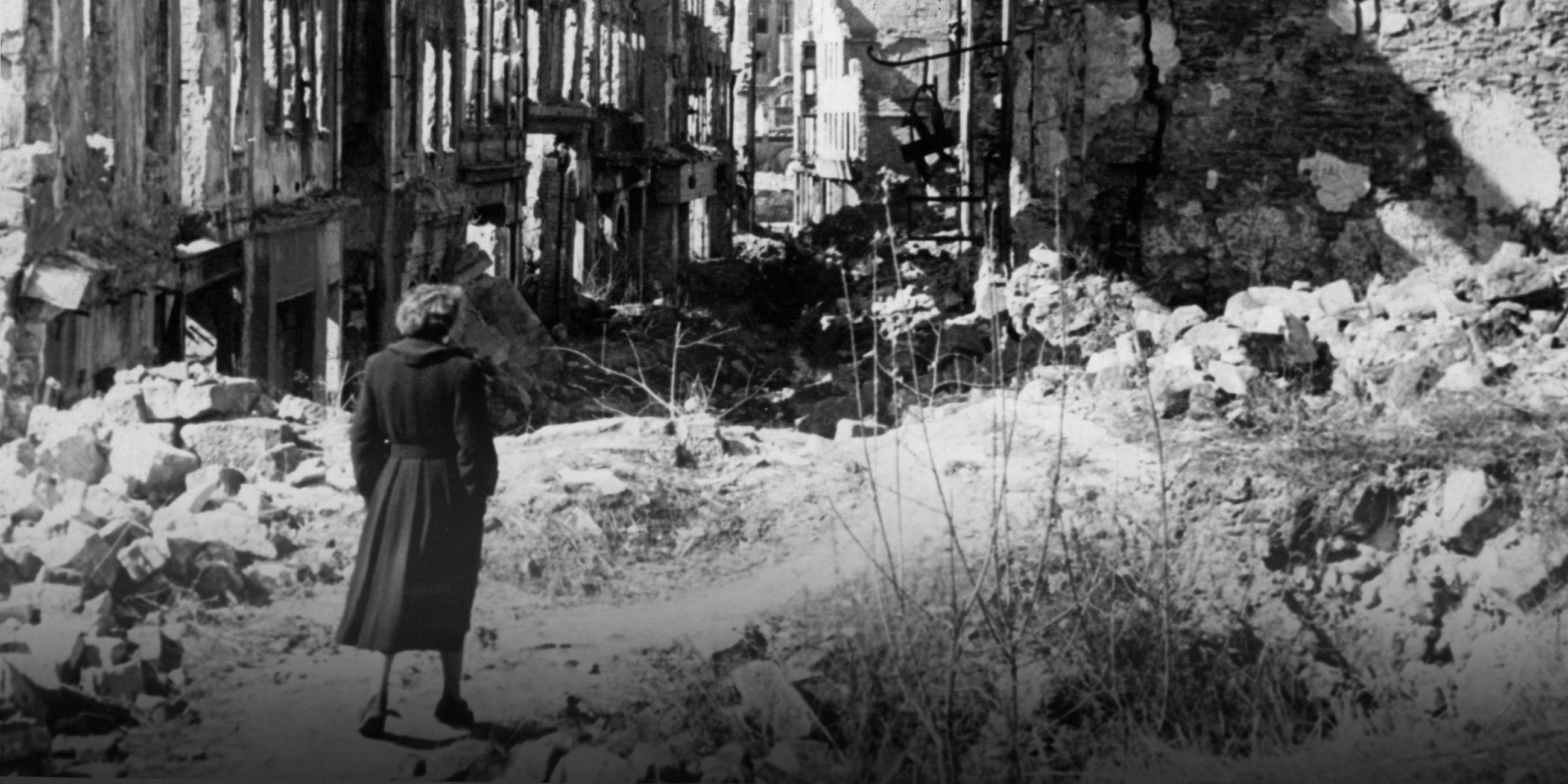 Eine Frau geht in einer Straße in Dresden an Häusern vorbei, von denen nach dem Zweiten Weltkrieg nur noch Ruinen geblieben sind