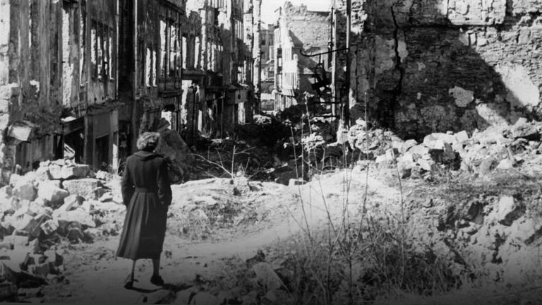 Eine Frau geht in einer Straße in Dresden an Häusern vorbei, von denen nach dem Zweiten Weltkrieg nur noch Ruinen geblieben sind