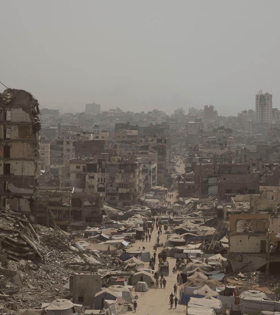Menschen gehen eine Straße entlang, die von Gebäuden umgeben ist, die durch israelische Bombardierungen im Gazastreifen zerstört wurden.