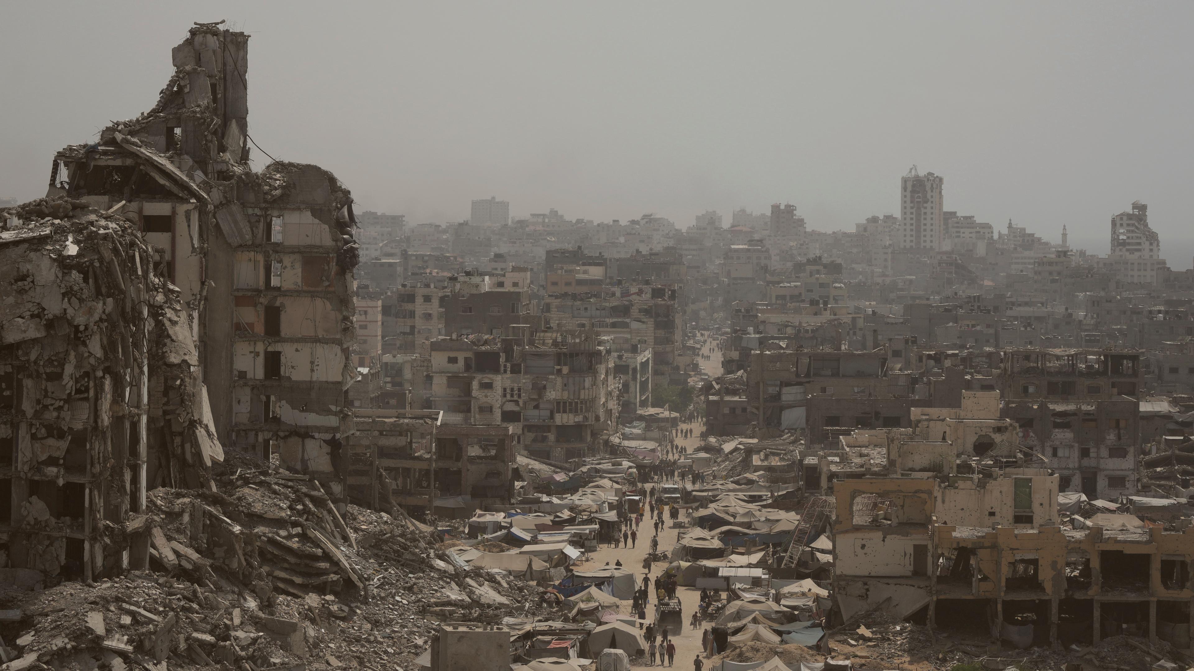Menschen gehen eine Straße entlang, die von Gebäuden umgeben ist, die durch israelische Bombardierungen im Gazastreifen zerstört wurden.