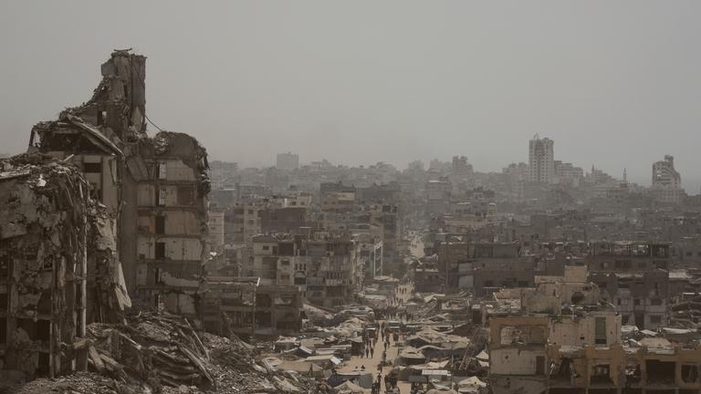 Menschen gehen eine Straße entlang, die von Gebäuden umgeben ist, die durch israelische Bombardierungen im Gazastreifen zerstört wurden.