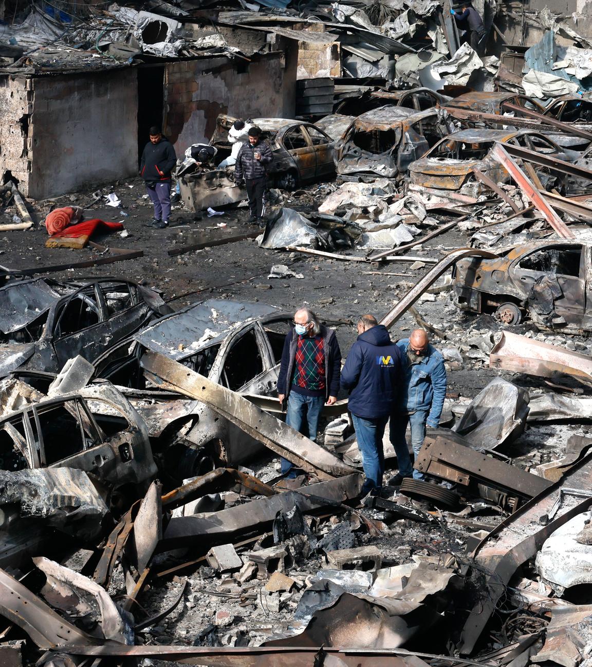 Menschen gehen zwischen den Trümmern eines Gebäudes und Autos hindurch, aufgenommen am 09.04.2026