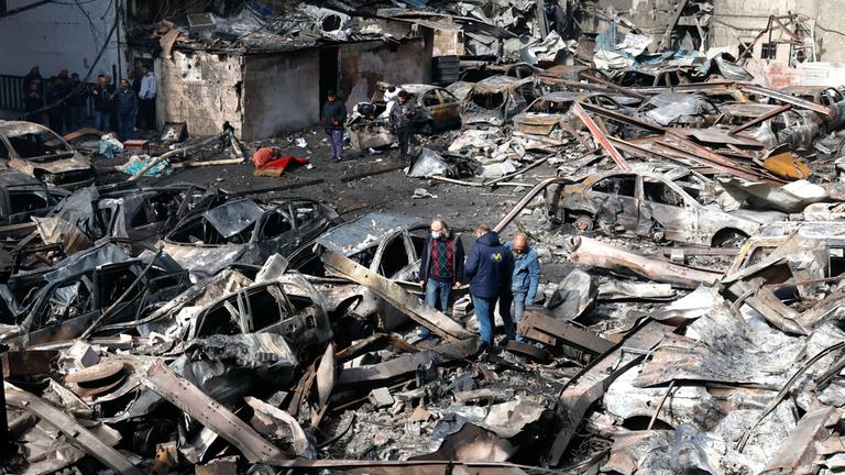 Menschen gehen zwischen den Trümmern eines Gebäudes und Autos hindurch, aufgenommen am 09.04.2026