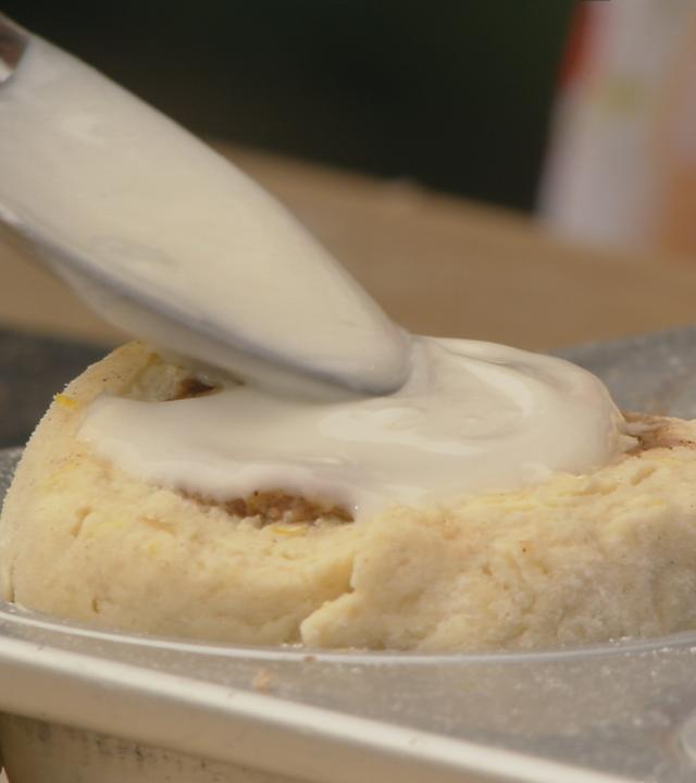 Löffel verteilt weiße Flüssigkeit auf Zimtstern-Schnecke