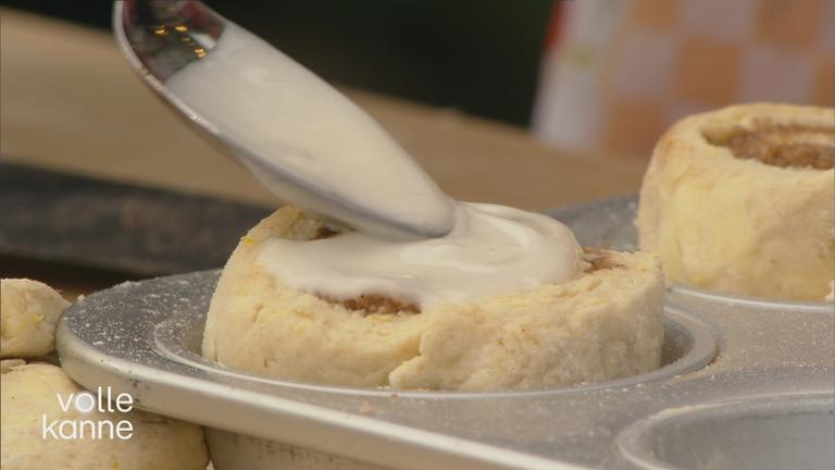 Löffel verteilt weiße Flüssigkeit auf Zimtstern-Schnecke