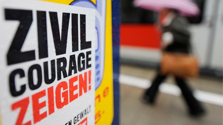 An einer Säule an einem S-Bahnhof hängt ein Plakat mit der Aufschrift "Zivicourage zeigen!"