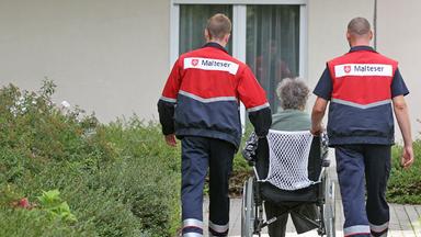 Zwei Zivildienstleistende betreuen eine Dialysepatientin im Rollstuhl in Leipzig.