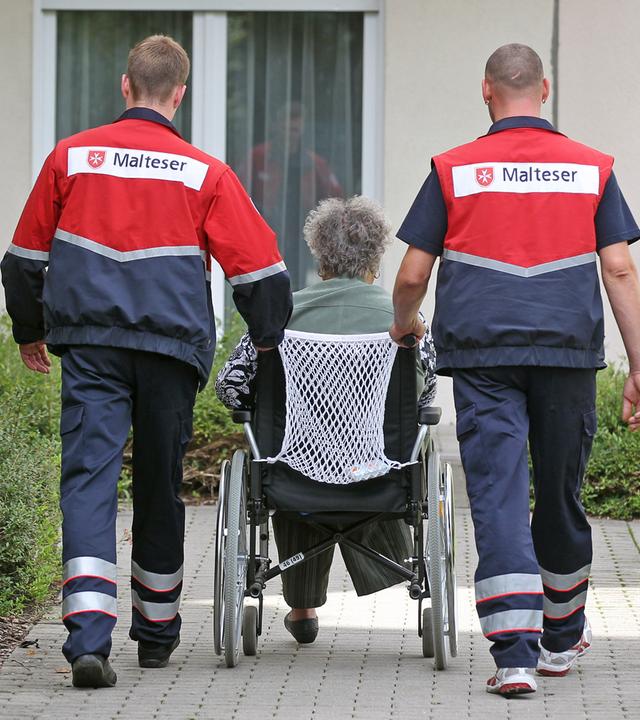 Zwei Zivildienstleistende betreuen eine Dialysepatientin im Rollstuhl in Leipzig.