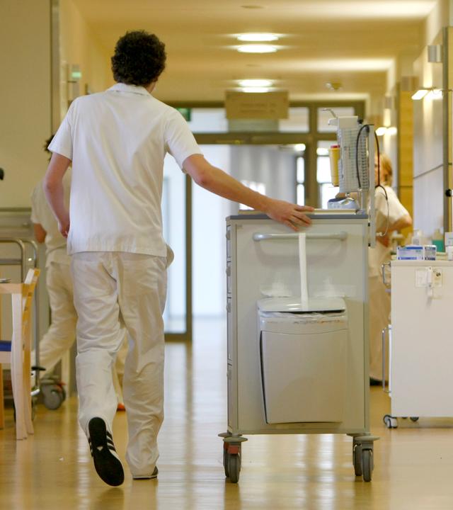 Ein Zivildienstleistender schiebt einen Medikamentenwagen über einen Flur in einem Krankenhaus