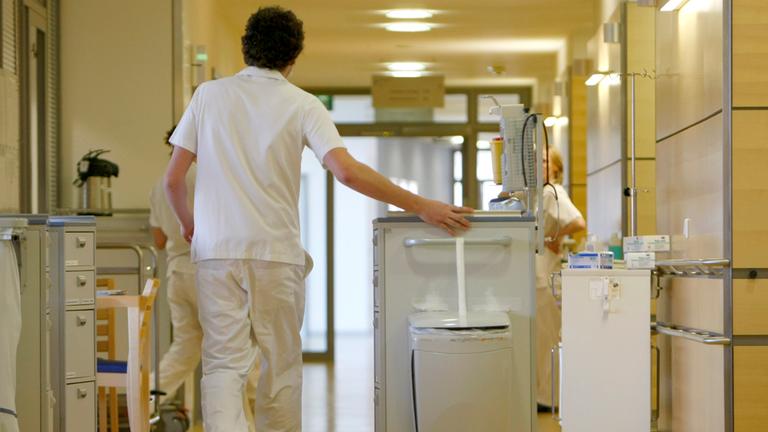 Ein Zivildienstleistender schiebt einen Medikamentenwagen über einen Flur in einem Krankenhaus