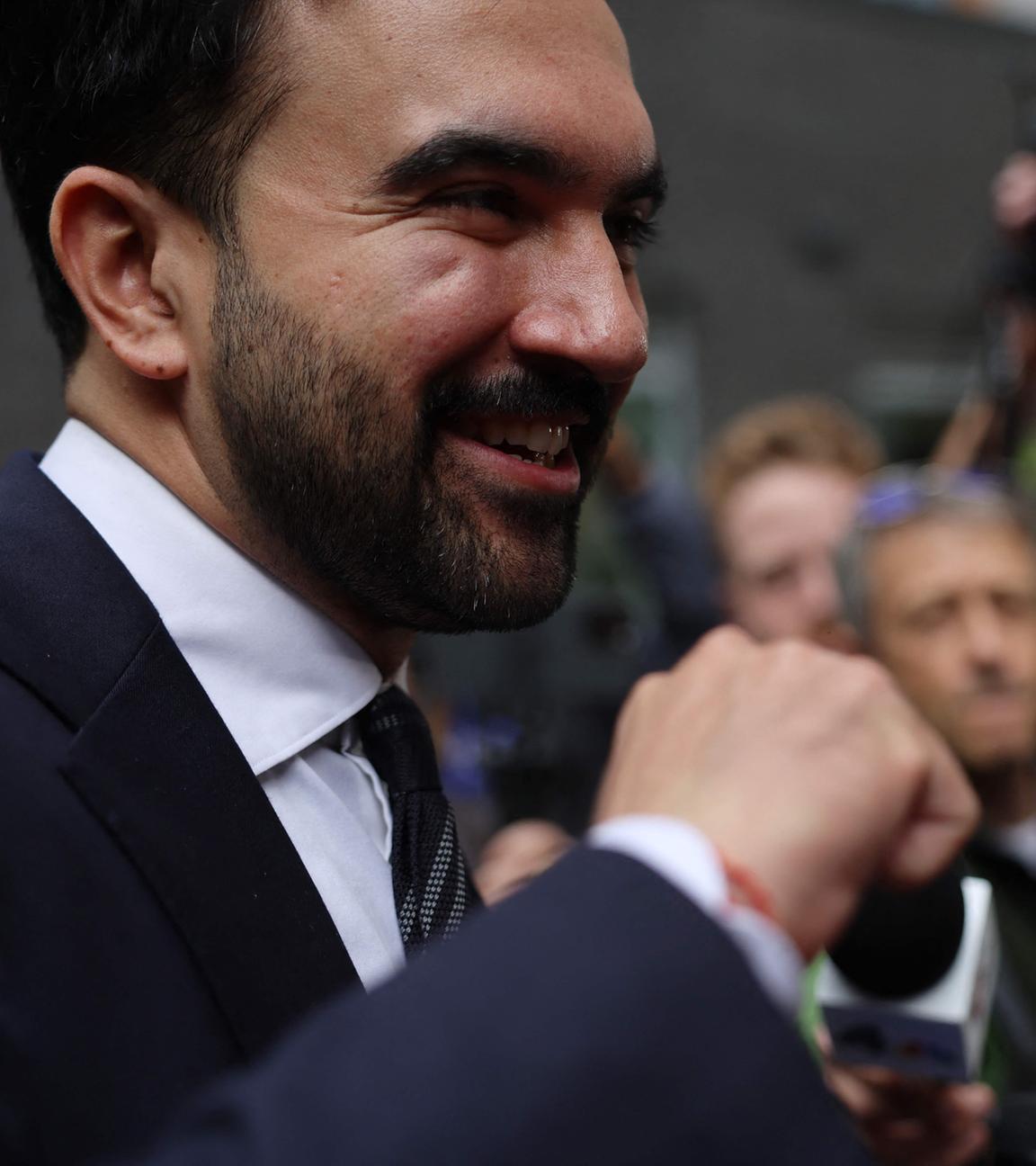 Zohran Mamdani lächelnd vor eine Gruppe Journalisten