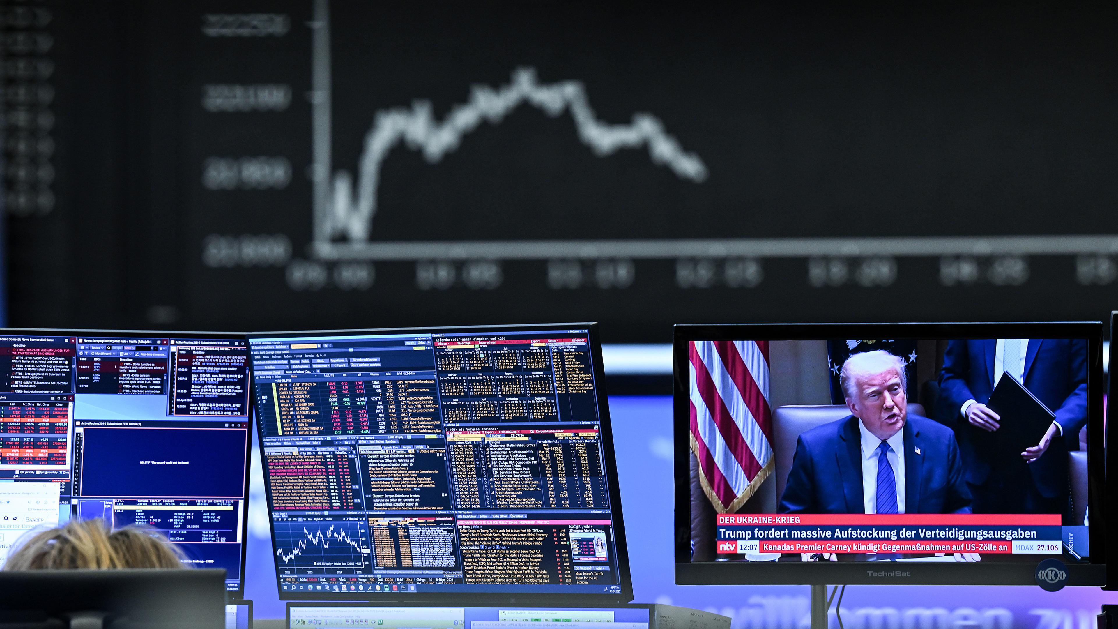 Hinter einem Fernsehmonitor, auf dem US-Präsident Donald Trump zu sehen ist, zeigt die Anzeigetafel mit der Dax-Kurve fallende Kurse. Das angekündigte Zollpaket von US-Präsident Trump hat die Aktienkurse kräftig ins Minus gedrückt