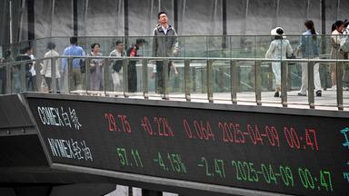 Menschen gehen am n09.042025 im Finanzviertel von Shanghai über eine Fußgängerbrücke mit einer Tafel mit Finanzmarktinformationen