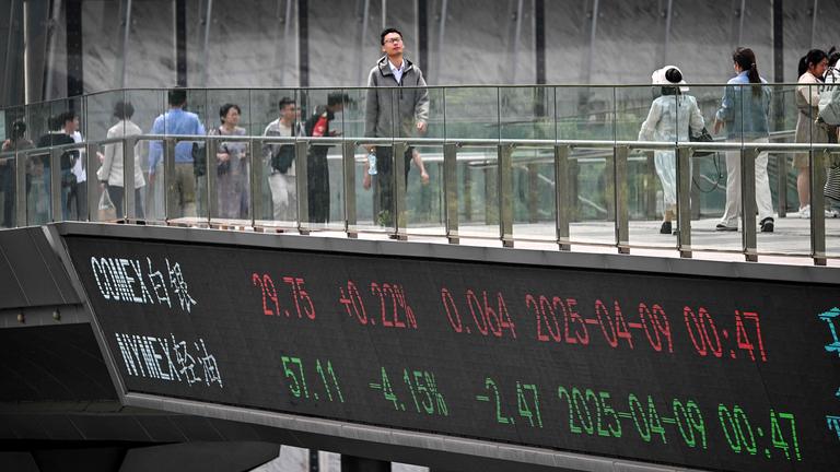 Menschen gehen am n09.042025 im Finanzviertel von Shanghai über eine Fußgängerbrücke mit einer Tafel mit Finanzmarktinformationen