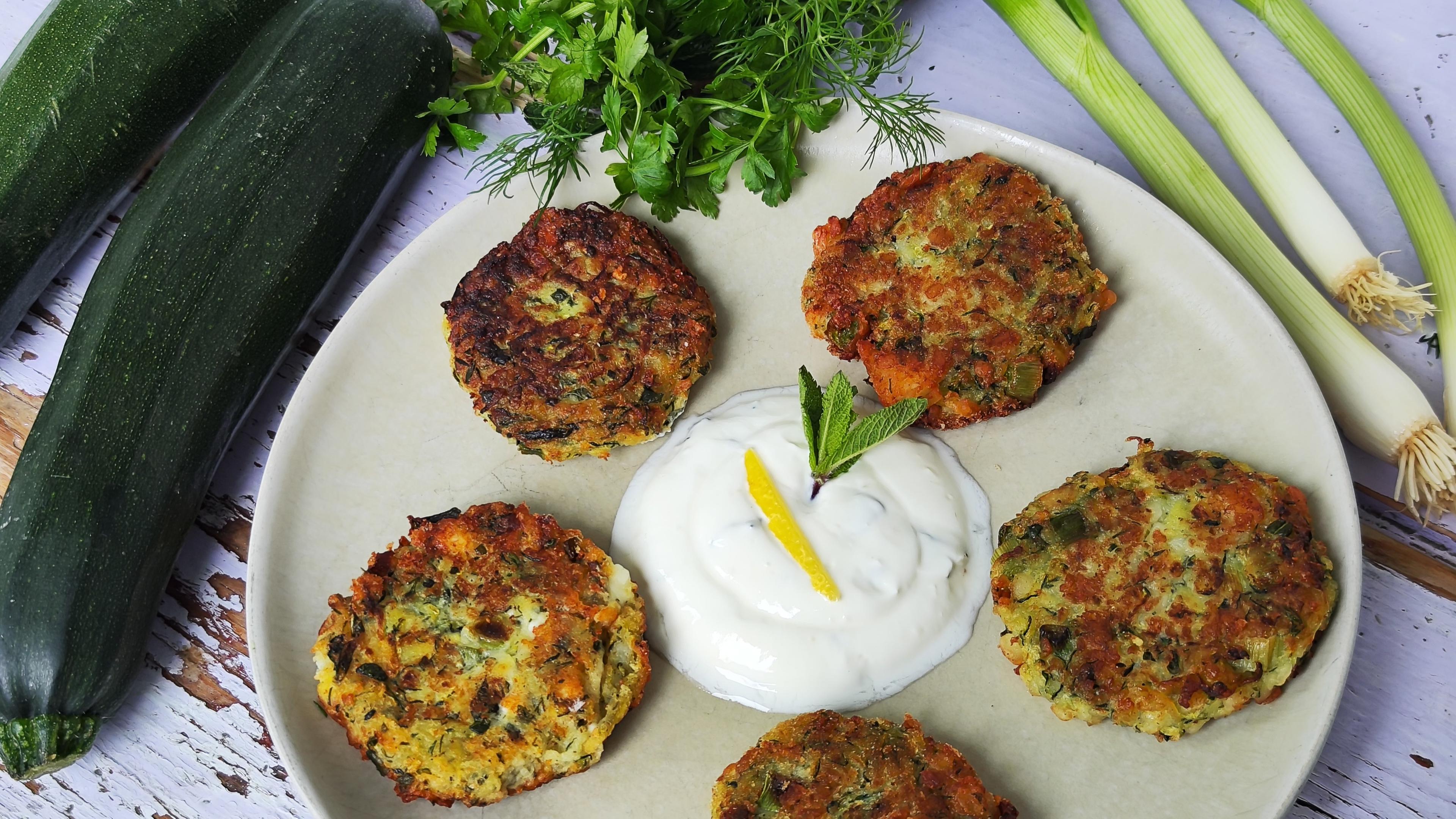 Zucchinipuffer mit Zitronen-Minz-Dip angerichtet auf einem hellen Teller.