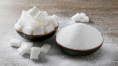 Zuckerwürfel und granulierter weißer Zucker in zwei braunen Schüsseln.