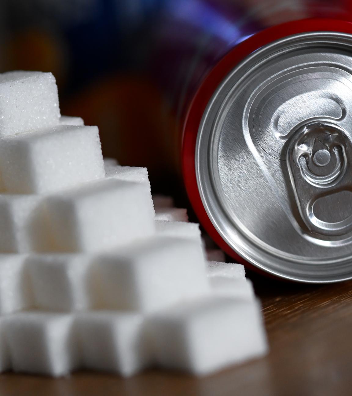 Eine Getränkedose mit einem Softdrink und zahlreiche Zuckerwürfel liegen auf einem Tisch. 