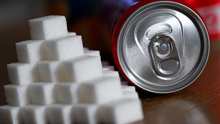 Eine Getränkedose mit einem Softdrink und zahlreiche Zuckerwürfel liegen auf einem Tisch. 