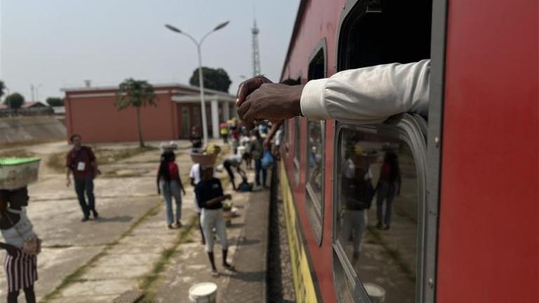 Ein Fenster des roten Benguela Express aus dem ein Arm rausgestreckt wird.