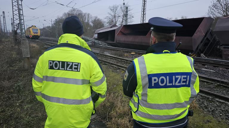 Niedersachsen, Elze: Einsatzkräfte der Bundespolizei stehen an den Gleisen neben umgekippten Schüttgutwagen.