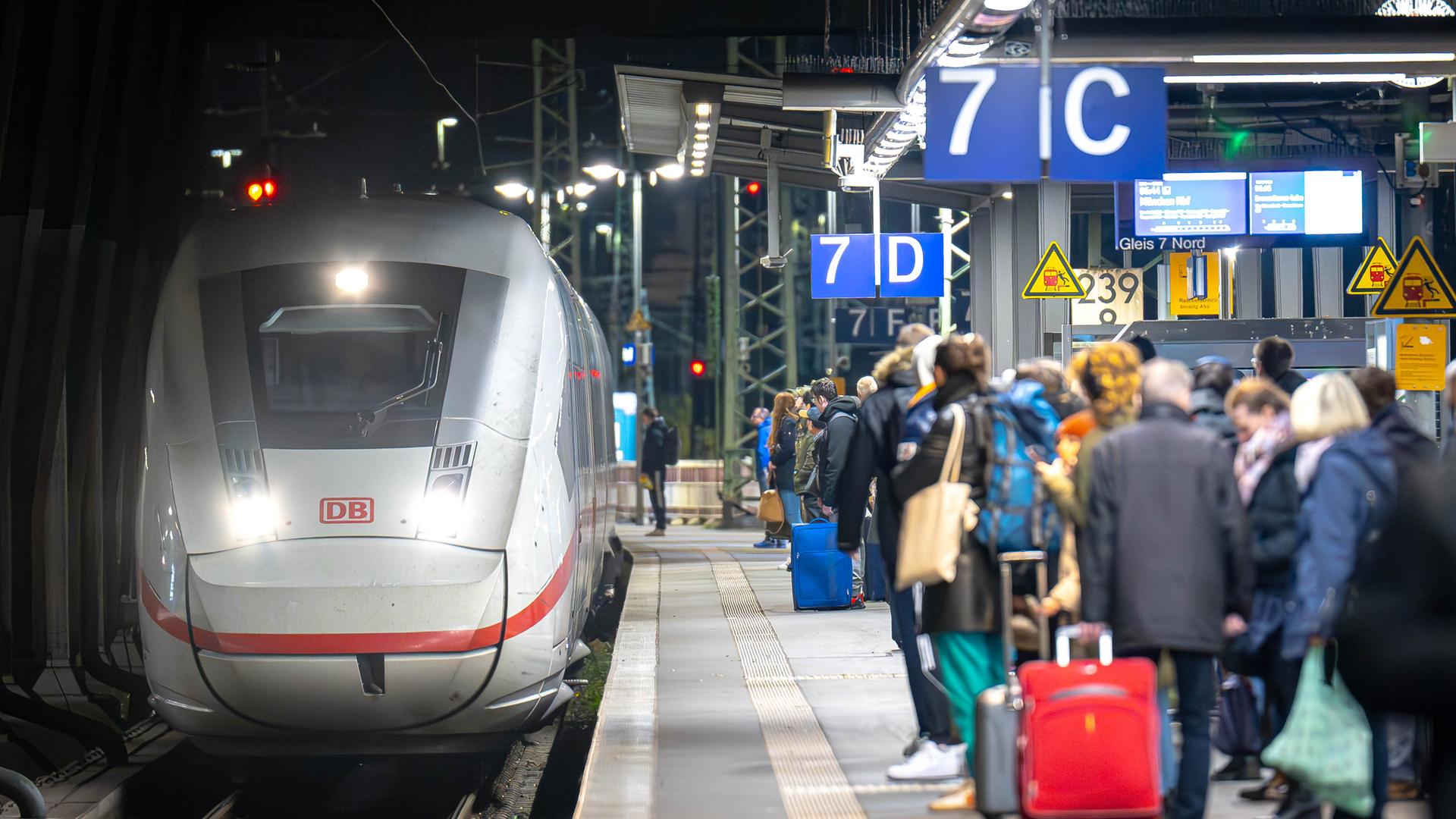 Zug fährt in Bahnhof ein und mehrere Menschen warten bereits am Gleis.
