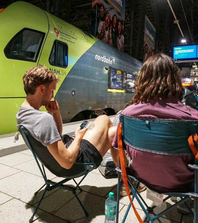 Reisende sitzen am Bahnsteig im Hamburger Hauptbahnhof