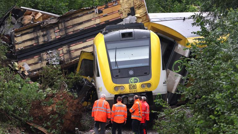 Der entgleiste Zug. Vor ihm stehen Arbeiter in Warnwesten. Rechts und Links von den Gleisen sind Büsche.