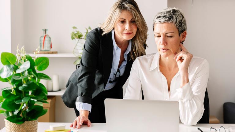 Zwei Frauen  in einem Gespräch vor einem Laptop auf dem Schreibtisch.