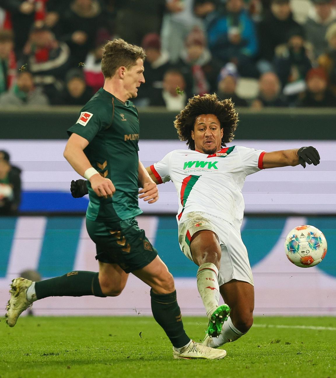 Augsburgs Han-Noah Massengo grätscht im Zweikampf mit Bremens Jens Stage in Richtung Ball um seinen Gegenspieler zu stoppen