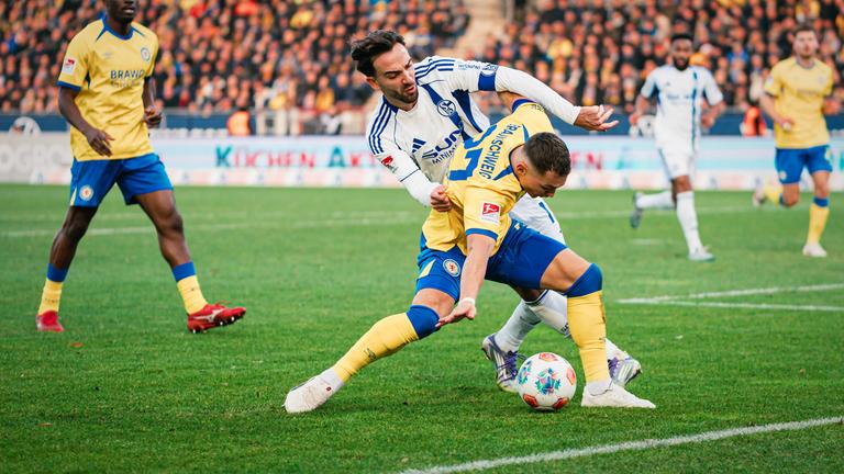 Braunschweigs Fabio Di Michele Sánchez wird in der Zweitligapartie zwischen der Eintracht aus Braunschweig und Schalke 04 von seinem Gegenspieler Karaman von hinten bedrängt