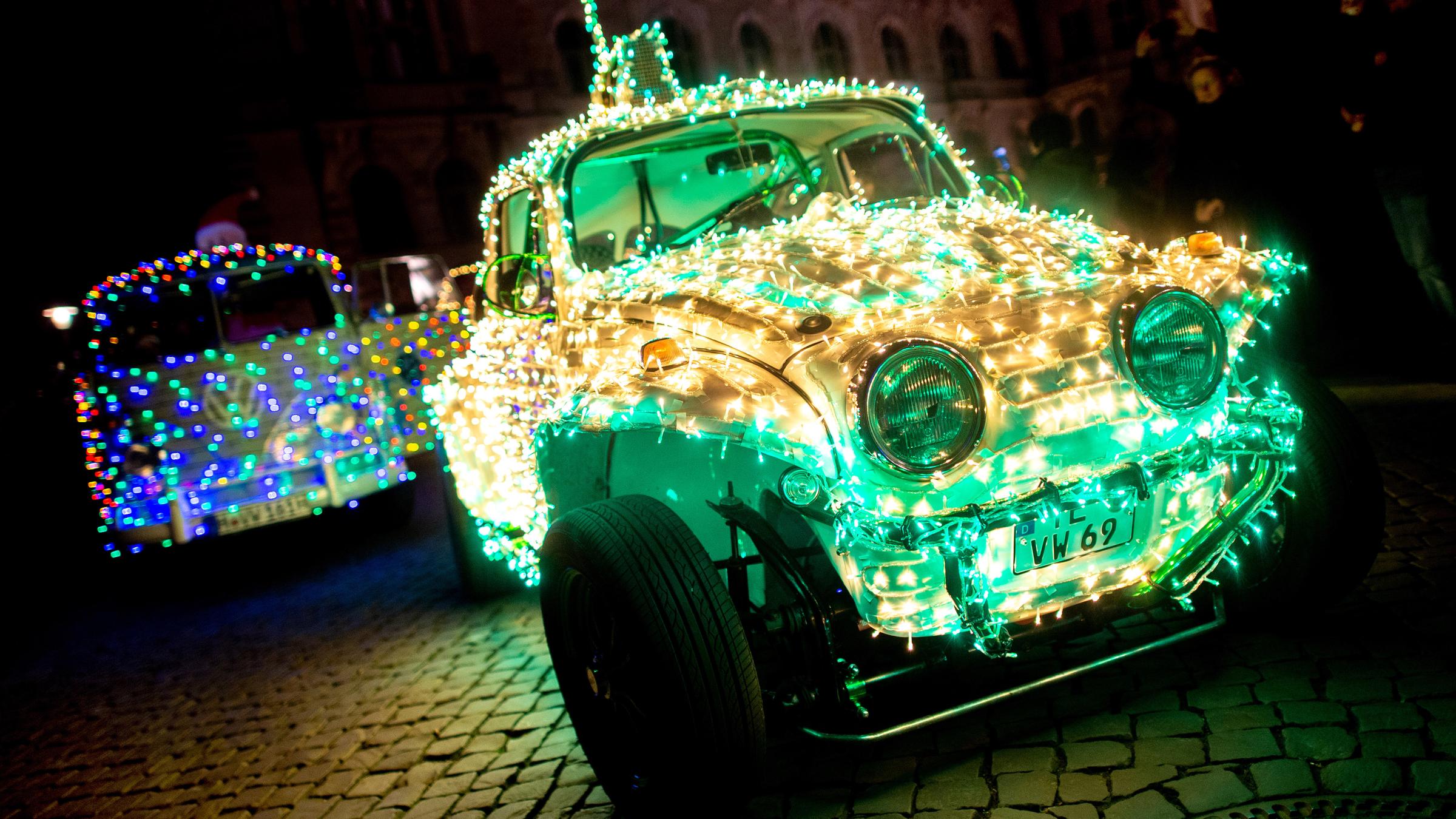 Ein mit Lichterketten geschmückter Volkswagen Käfer und ein Volkswagen T1 stehen auf dem Trammplatz.