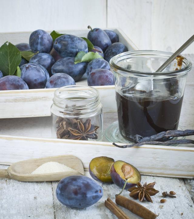 Frische Zwetschgen mit Gewürzen wie Vanille und Zimtstangen sowie ein mit Mus gefülltes Glas.